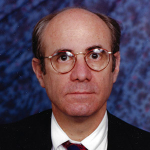 Dr. Liegner's face with glasses on looking straight at the camera. He has a suit, white shirt, and tie.